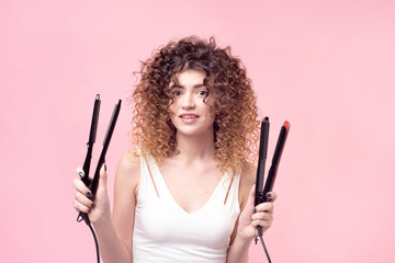 Beautiful woman with amazing curls in white shirt holds styling accessories in hand. Hair styling...
