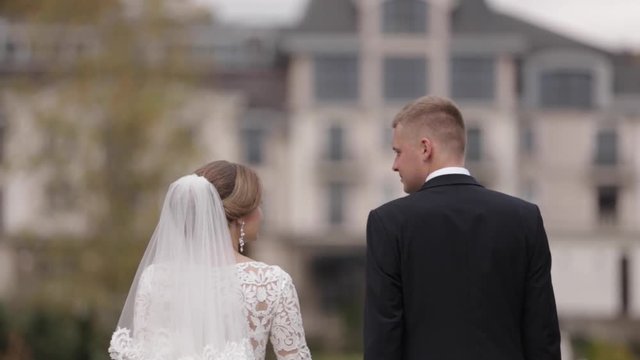 Happy newlyweds walking in the park. Elegant bride and handome groom outside