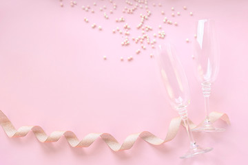 Champagne glasses with scattered white pearls and golden tape on pink background. Celebrate party concept, minimal style. Greeting card for Christmas, birthday, wedding. Flat lay, top view.