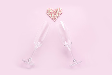 Champagne glasses with white pearls in shape of heart on pink background. Celebrate party concept, minimal style. Greeting card for Valentine's Day, wedding. Flat lay, top view.
