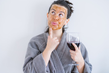 Beautiful woman wearing cosmetic facial mask as skincare treatment drinking glass of wine serious...
