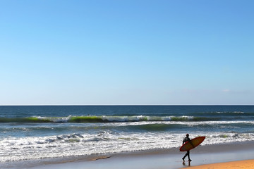 Fototapeta na wymiar Silhouette of a surfer walking near the edge of the ocean
