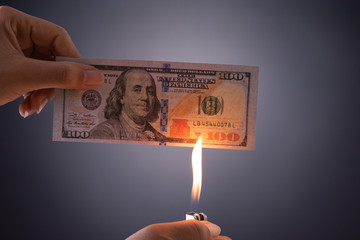 Woman hand holding burning burning dollar cash money over black background - business finances,...