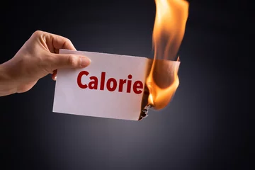 Foto op Plexiglas Woman hand holding a burning piece of paper with the word calories. Healthcare concept. © Siam