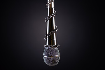Microphone with a chain, depicting the idea of freedom of the press or freedom of expression on dark background. World press freedom day concept.