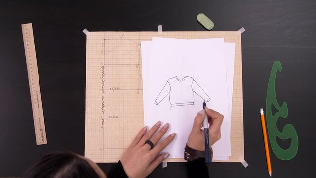 Designer hands who paint a pattern for sewing sweatshirt. Top view. 