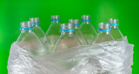 Bottlenecks of a pack of 8 empty and recyclable plastic water bottles, with no caps, blue seal, inside a plastic bag, on a  colored vivid green background. garbage, Reuse, Eco-Friendly.