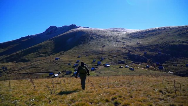 Hiker man with backpack walking to the plateau at the foot of snowy and icy mountains. Koroglu Mountains in Turkey