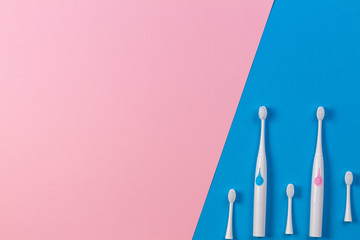 Two electric toothbrushes with three brush heads on blue and pink background. Top view