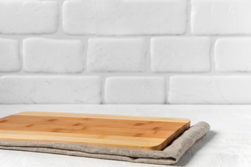 Fototapeta na wymiar Kitchen with cutting board on table, with linen tablecloth against the background a brick wall.