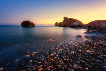 Aphrodite's Rock beach, Petra tou Romiou, the birthplace of Goddness Aphrodite, Paphos, Cyprus. Amazing sunset seascape of Love beach with rocks and sea pebbles, travel background, tourist location