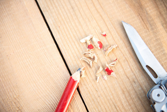 Background with tools. Pencil red sharpened with a folding knife lies on a wooden background
