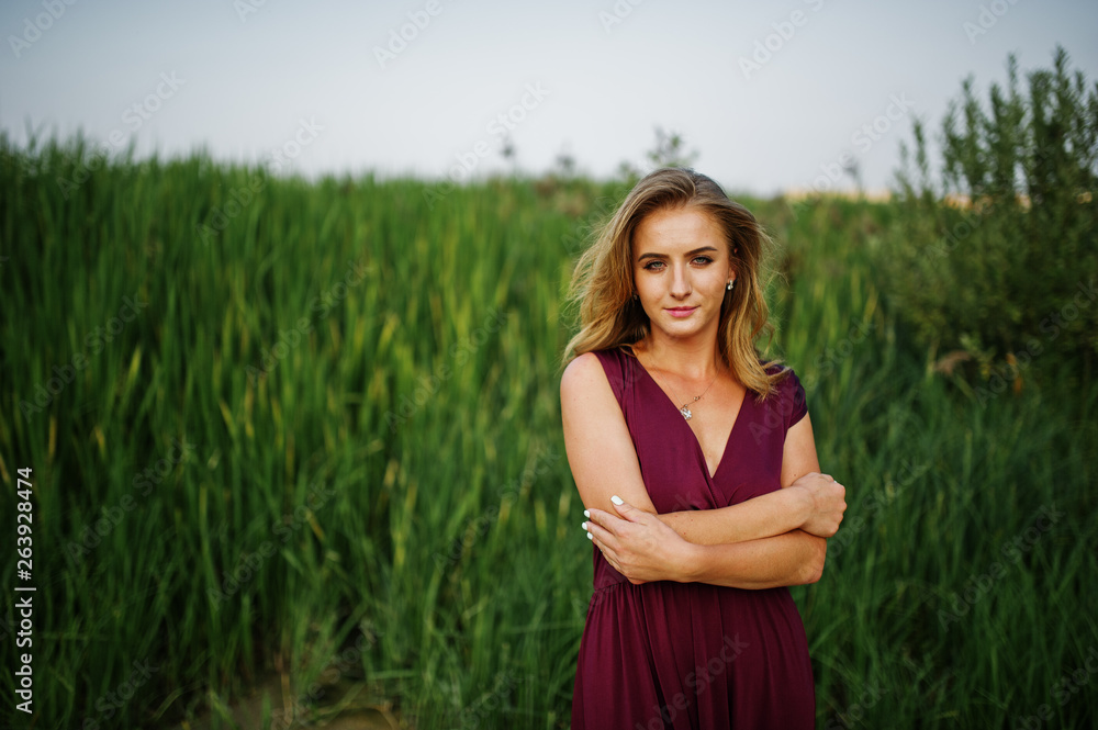 Wall mural Blonde sensual woman in red marsala dress posing in the reeds.