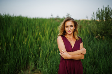 Blonde sensual woman in red marsala dress posing in the reeds.