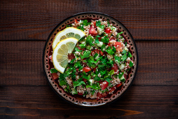Tabbouleh salad on a plate, dark wooden background. Oriental, vegetarian salad, traditional cuisine. Top view.