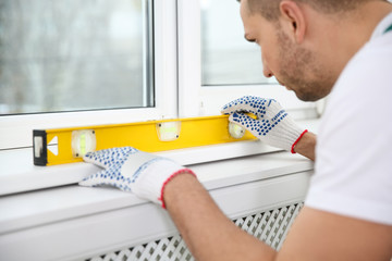 Construction worker using bubble level while installing window indoors