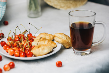 healthy light breakfast. sweet cherry with croissants on a plate. bouquet in a vase with spikelets of wheat. tea in a cup. Straw hat. proper nutrition for a slim figure. raw foods vegetarianism. diet