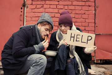 Poor young couple with HELP sign and bread on dirty street