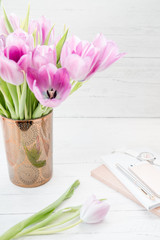 Feminine workspace. Bright and airy desk top with notepad and pink tulips. Vertical.