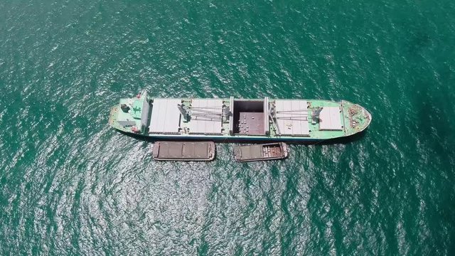 Aerial birds eye view above large shipping taker floating in turquoise blue reef waters. Tilting up to hazy ocean skyline as other various ships reveal along the horizon.