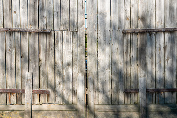 Tekstura drzwi wejściowych do stodoły. Na deskach widać ślad czasu poprzez równoległe pęknięcia w drewnie. Widoczne stare zardzewiałe gwoździe. Widoczne zawiasy