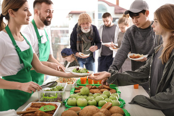 Volunteers giving food to poor people indoors