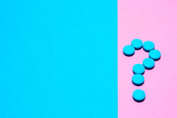blue pills laid out in a question symbol on a paper background of blue and pink with copy space