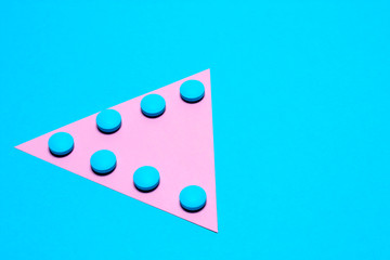 blue tablets laid out in the form of a triangle or an arrow on a paper background of blue and pink with copy space
