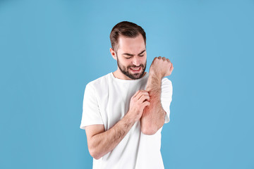 Young man scratching hand on color background. Allergies symptoms