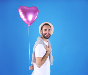 Portrait of young man with heart shaped balloon on color background