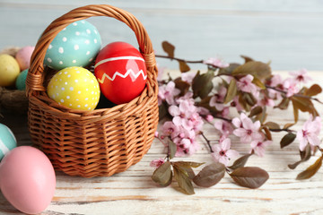 Painted Easter eggs in wicker basket and blossoming branches on wooden table
