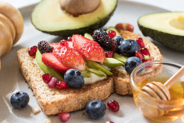 Avocado toast with berries topping on a plate on white wooden background