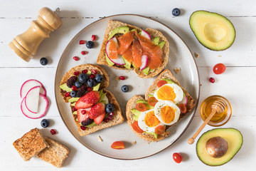 Avocado toast with different topping including salmon fish, eggs, berries, healthy and organic food, breakfast meal on white wooden background