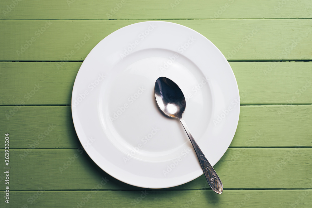 Poster white plate and a fork with a spoon on a green wooden table background.
