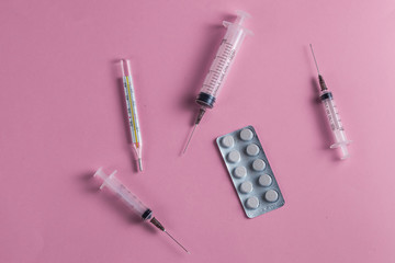 close up of medical pills, needles of a syringe, thermomiter on pink table, sick man's table. first helper