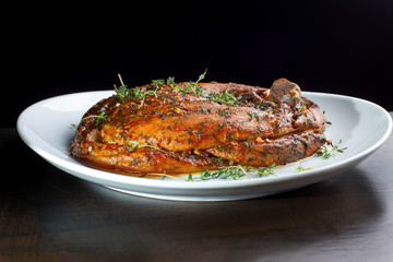 Roast pork knuckle on white plate, sprinkled with rosemary.