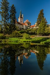Fototapeta na wymiar Pruhonice, Czech Republic - April 22 2019: Scenic landscape of famous romantic Pruhonice castle, standing on green hill in park, sunny spring day, blue sky, trees, reflection in water, vertical image