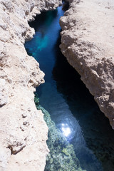 The reflection of the sunblock in a small creek of a blue-blue color flowing between light yellow gray brown brown stones. Vertical photo