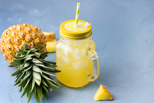 Tasty Pineapple Cocktail or Juice in Glass Jar with Straws and Two Pineapples on a Blue Background Ice Cube