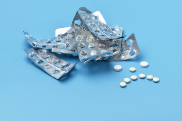 Sad face with white pills. A lot of empty packages of pills on a blue background, lined with a sad grimace of pills