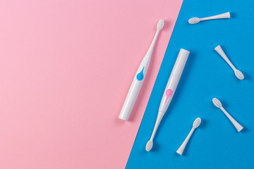Two electric toothbrushes with brush heads on blue and pink background. Top view