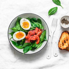 Delicious brunch - spinach, smoked salmon, soft boiled egg on a light background, top view. Healthy eating diet concept