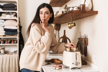 Picture of satisfied brunette woman 30s making breakfast with toasts at home