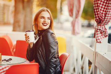 young and pretty girl sitting in a summer city and drinking a coffee