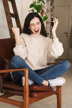 Photo of excited caucasian woman 20s wearing earphones singing while listening to music indoor