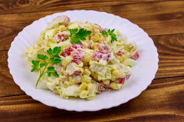 Salad with crab sticks, sweet corn, chinese cabbage, eggs and mayonnaise on wooden table