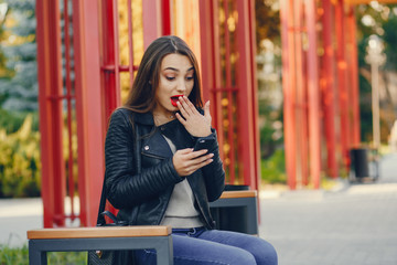 young and pretty girl sitting in a summer city with phone