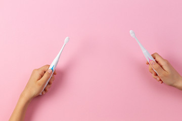 Kid hands with electric toothbrushes on pink background