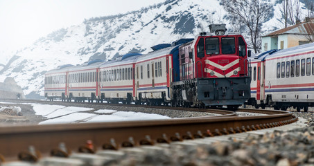 Fototapeta premium Train at snow covered railway line in snowy valley between the mountains.