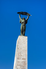 Hungary, Budapest, Gellert Hill: Famous bronze Liberty Statue or Freedom Statue from below above the city center of the Hungarian capital with blue sky in the background - travel history liberation
